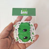 Image of a hand holding a Best Buds Sticker Pack. The stickers are packaged in a clear bag with an emerald green logo and seal. Includes several stickers. 